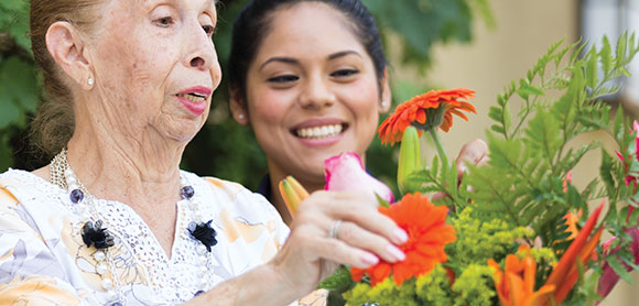 image of an elderly lady with flowers alongside a young woman. Both smiling.